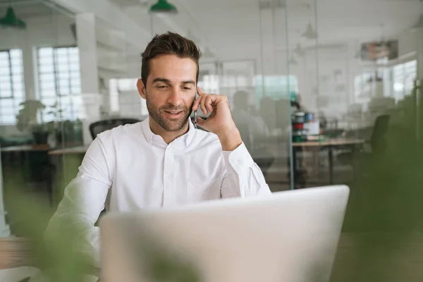 Joven Hombre Negocios Sonriente Trabajando Portátil Hablando Teléfono Celular Mientras — Foto de Stock