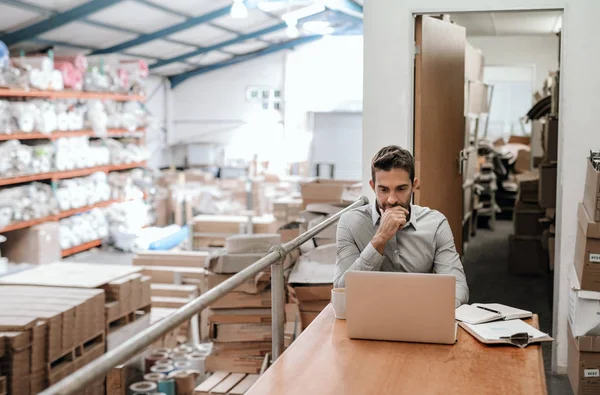 背景に在庫の棚を持つカーペット倉庫の机に座っている間 ラップトップで作業するマネージャー — ストック写真