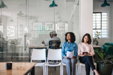 Bir ofisin önünde birlikte sandalyede oturan iki genç kadın mülakat randevularını bekliyor.