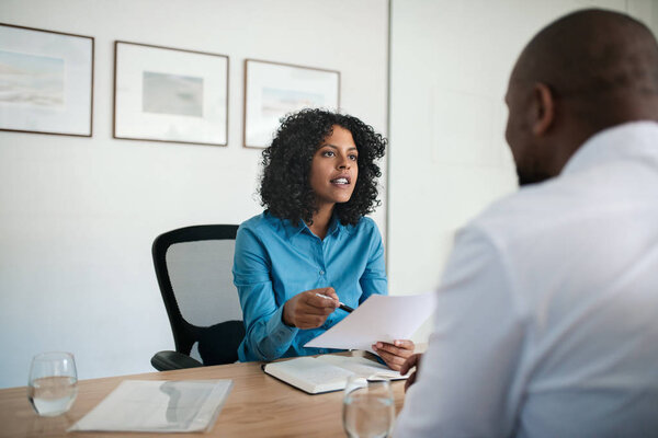Manager asking questions and reading a resume with a new job applicant while sitting at her desk in an office