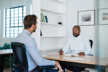 Afro-Amerikan ofis yöneticisi masasında otururken bir meslektaşı ile notlar ve evrak üzerinden gidiyor