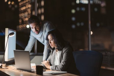 İki odaklanmış genç işadamları gece geç saatlere kadar mesai yaparken bir ofis masasında dizüstü bilgisayar kullanıyor