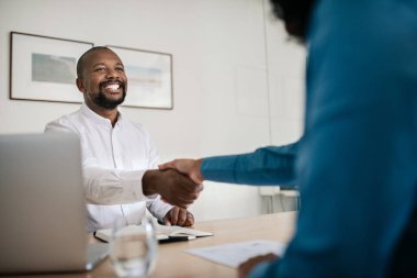 Gülümseyen Afro-Amerikan yöneticisi bir görüşmeden sonra bir iş başvuru ile el sıkışma ofis masasında oturan
