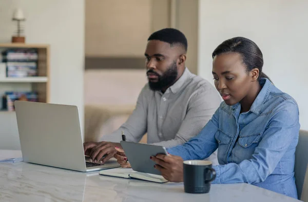 年轻的非洲裔美国夫妇坐在餐桌旁 用笔记本电脑和数字平板电脑处理他们的家庭财务问题 — 图库照片