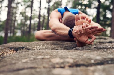 Fit adam bir çam ormanında yoga yaparken diz poz yaparken bir kaya üzerinde tek başına oturan