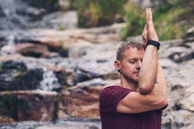 Ormanda bir şelale tarafından tek başına yoga yaparken kartal poz yaparken kayaların üzerinde duran fit adam