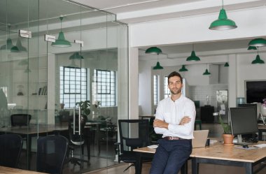 Kollarıyla eğilen genç bir işadamının portresi büyük modern bir ofiste masaya yaslandı