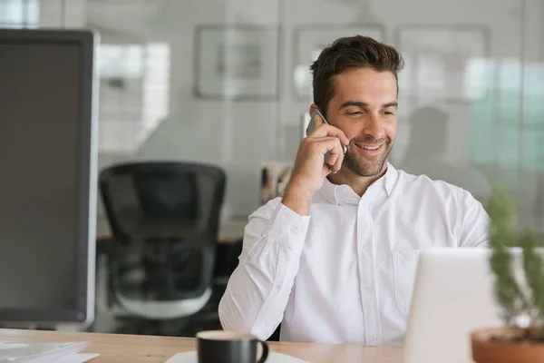 Усміхнений Молодий Бізнесмен Сидить Своїм Столом Сучасному Офісі Розмовляє Мобільному — стокове фото