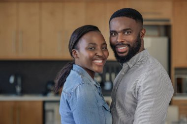 Mutfaklarında birbirlerine yakın dururken gülümseyen sevecen genç Bir Afrikalı-Amerikalı çiftin portresi