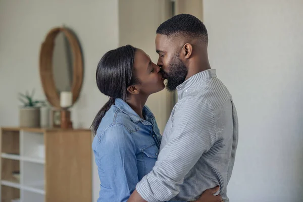 ロマンチックな若いアフリカ系アメリカ人のカップルは お互いの腕の中に立って 自宅のリビングルームでキス — ストック写真