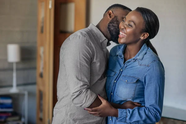 彼の笑う妻に自宅のリビングルームで頬にキスを与える若いアフリカ系アメリカ人の男性 — ストック写真