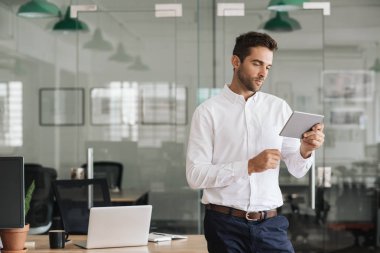 Odaklanmış genç işadamı dijital tablet ile online çalışan büyük bir modern ofiste tek başına ayakta