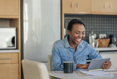 Genç Afrikalı Amerikalı kadın dijital tablet ile evde mutfak masasında çalışırken gülüyor