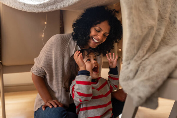 Cute little girl laughing while sitting in a blanket fort with her mother on their living room floor at home