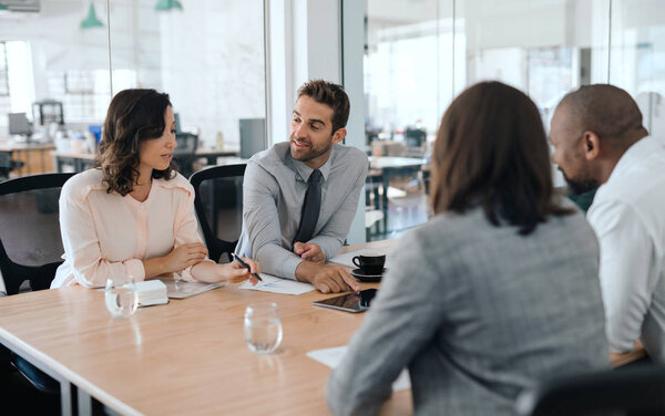 Smiling group of diverse businesspeople sitting together around a table in an office boardroom discussing work