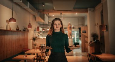 Akşam bir restoranda çalışırken yiyecek tepsileri taşıyan gülümseyen genç bir garson portresi