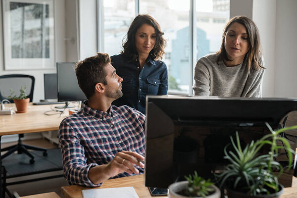 Группа молодых дизайнеров, работающих за компьютером вместе за столом в своем стартапе
