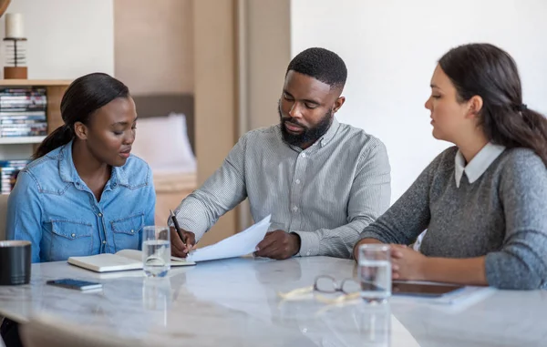 年轻的非洲裔美国人夫妇和他们的财务顾问坐在客厅的桌子旁签署文件 — 图库照片