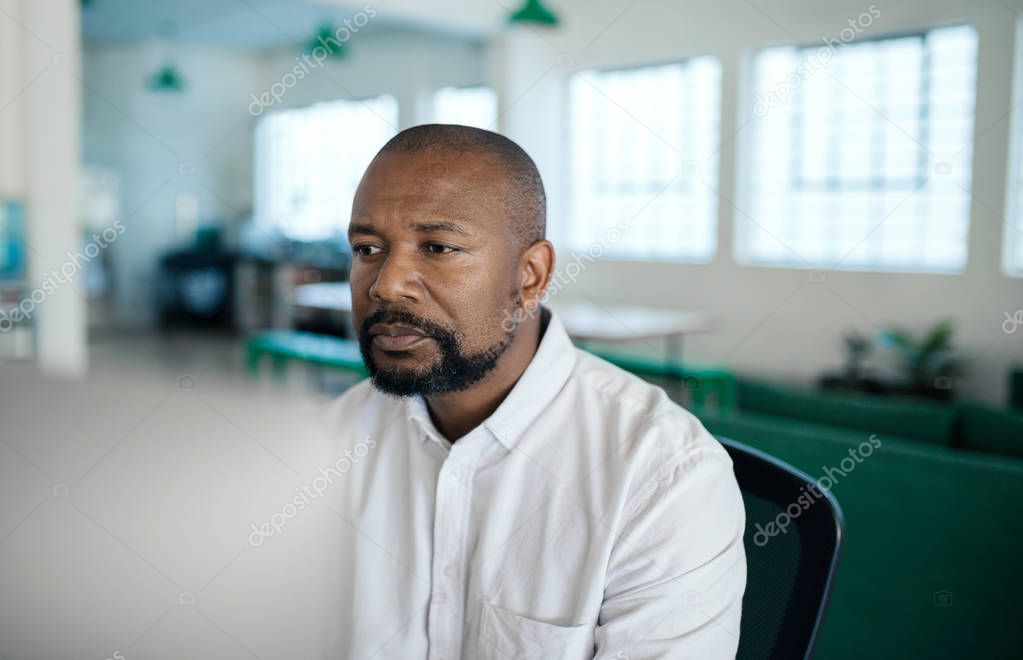 Focused mature African American businessman working on a computer while sitting at his office desk in the late afternoon