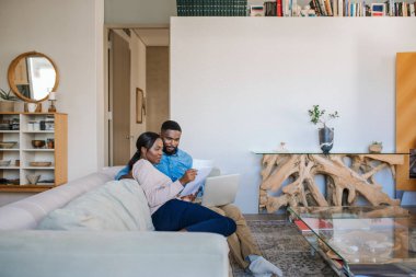 Oturma odasındaki kanepede oturan genç Afrikalı Amerikalı çift internette faturalarını ödüyor.