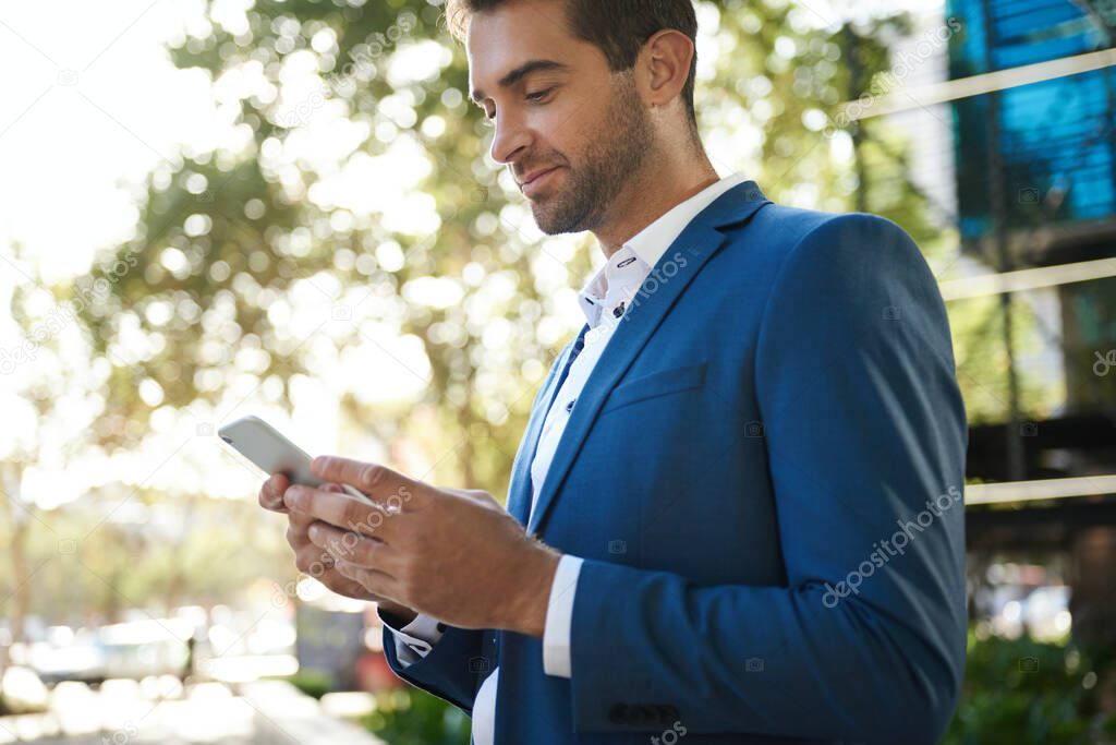 Young businessman sending a text message on his cellphone while standing outside in the city on a sunny afternoon