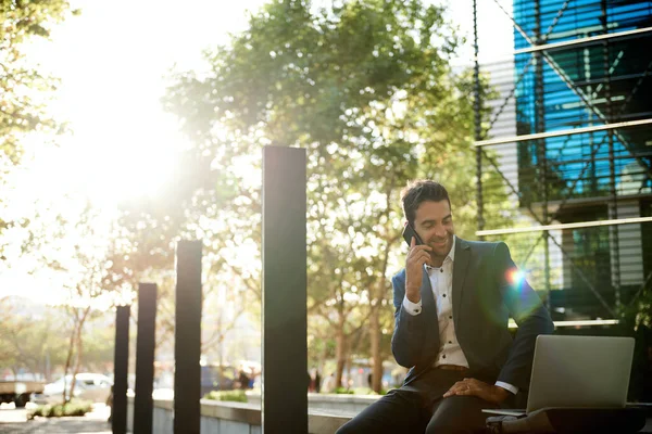 Jovem Empresário Sorrindo Trabalhando Laptop Falando Seu Celular Enquanto Sentado — Fotografia de Stock