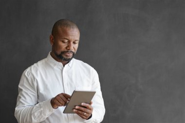 Olgun bir Afro-Amerikan işadamı, boş bir ofis tahtası önünde dururken dijital tablet kullanıyor.