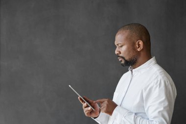 Olgun Afrikalı Amerikalı işadamı boş bir ofis tahtası önünde dururken dijital tablet üzerinde çalışıyor.
