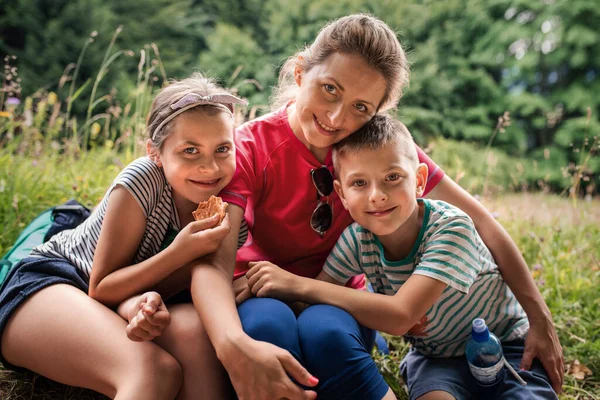 笑顔の母親と彼女の2人のかわいい子供の肖像画彼らの家族のハイキングから休憩を取るパスに座って — ストック写真