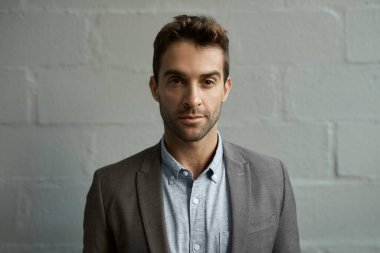 Odaklanmış genç bir iş adamının portresi bir ofiste beyaz tuğla bir duvarın önünde tek başına duruyor.