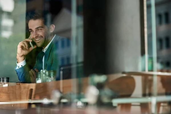 Gülümseyen Genç Bir Işadamı Kafenin Penceresinde Otururken Cep Telefonuyla Gülümsüyor — Stok fotoğraf