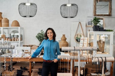 Gülümseyen Asyalı genç bir bayan girişimcinin portresi moda dükkanında tezgahın önünde duruyor.