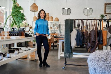 Gülümseyen Asyalı genç bir bayan girişimcinin portresi. Moda dükkanında masa başında duruyor.