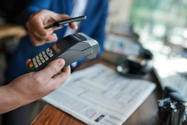 NFC terminalini kullanarak bir müşterinin ödemesini akıllı bir telefonla almak için bir kafe garsonunun yakın çekimi.