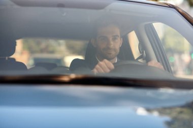 Genç bir adam sabah işe gitmek için işe giderken şehirde bir cadde boyunca araba kullanıyor.