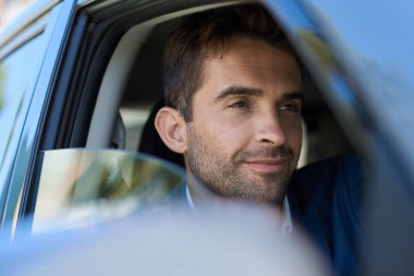 Gülümseyen genç bir adam işe gitmek için sabah işe giderken arabasıyla şehrin içinden geçiyor.