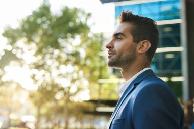 Güneşli bir öğleden sonra şehrin dışında ceketli, kendinden emin genç bir iş adamının profili.