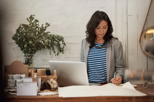 Genç Asyalı kadın moda dükkanının kasasında duruyor notlar yazıyor ve bir dizüstü bilgisayar üzerinde çalışıyor.