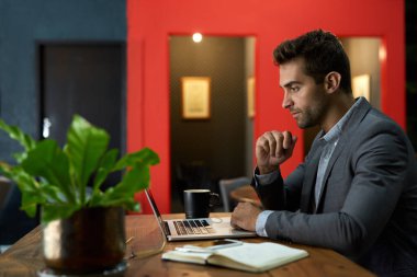 Saatler sonra sessiz bir ofiste masasında tek başına otururken bilgisayarla çalışan odaklanmış genç bir iş adamı.