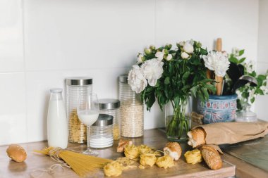 Beyaz Doğrama Kurulu, çiçekler ile modern mutfak duvar fayans, bıçaklar, makarna, ekmek. Beyaz beyaz üst arka plan ve malzemeler ile modern bir mutfak duvar fayans