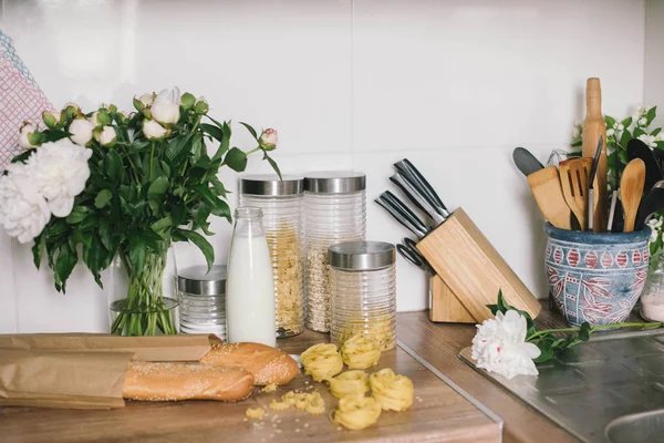 White tiles wall modern kitchen with chopping board,flowers,knifes,pasta,bread. White tiles wall modern kitchen with white top background and ingredients