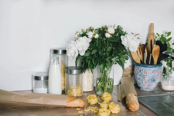 White tiles wall modern kitchen with chopping board,flowers,knifes,pasta,bread. White tiles wall modern kitchen with white top background and ingredients