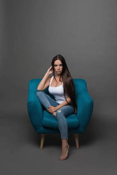 Güzel uzun saçlı Genç güzel kadın portre portre. Oturma ve stüdyoda poz. Trendy, neşeli, modern, şık, gri arka plan üzerinde izole Eyewear kadın portresi.