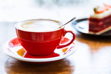 Ahşap bir masanın üzerindeki kırmızı bir fincan kahveyi kapat. Arka planda çilekli siyah bir tabak var.