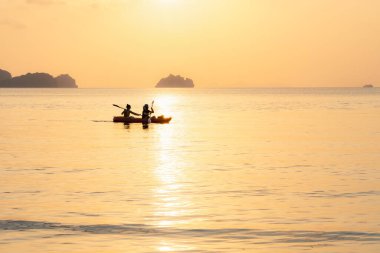Denizde kayak yapan çift adaların arka planında ve altın gün batımında