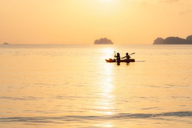 Denizde kayak yapan çift adaların arka planında ve altın gün batımında