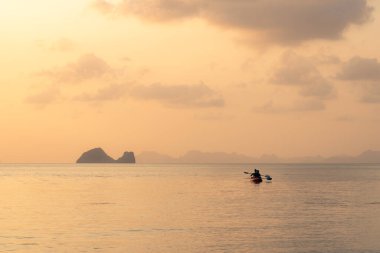 Denizde kayak yapan çift adaların arka planında ve altın gün batımında