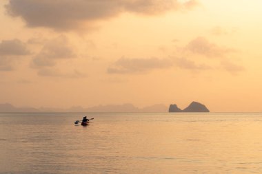 Denizde kayak yapan çift adaların arka planında ve altın gün batımında