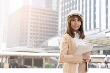 Büyük şehirde bina önünde mutluluk güzel mühendis giyim beyaz emniyet kask ayakta.