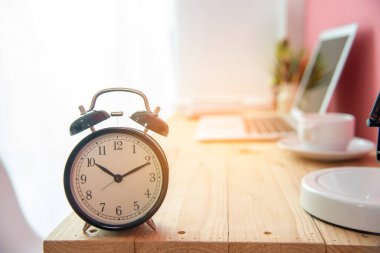 İş zamanı bitiş zamanı iş konseptinde çalar saat. Alarm uyanık. Randevu zaman çizelgesi. Kahve fincanı ve yumuşak güneş ışığı olan dizüstü bilgisayarlı ahşap masa üzerindeki seçici odaklanma saati.